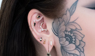 Close-up of an ear with multiple earrings and tattoos on a shoulder